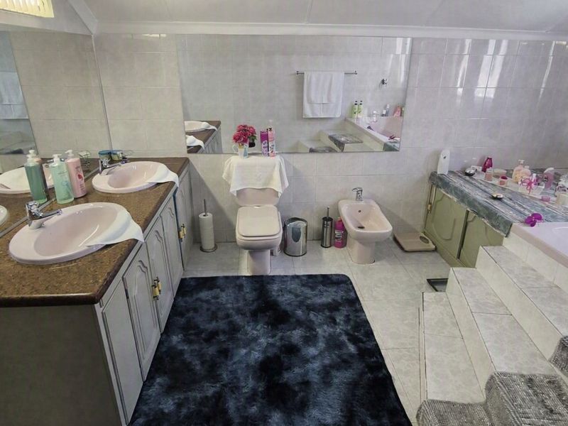 Spacious bathroom featuring a double vanity, built-in bathtub, bidet, and toilet with neutral wall tiling and a large vanity mirror.
