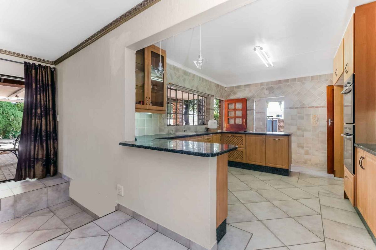 A functional kitchen featuring wooden cabinetry, granite countertops, and tiled flooring, with an open-plan layout connecting to the adjacent living area.