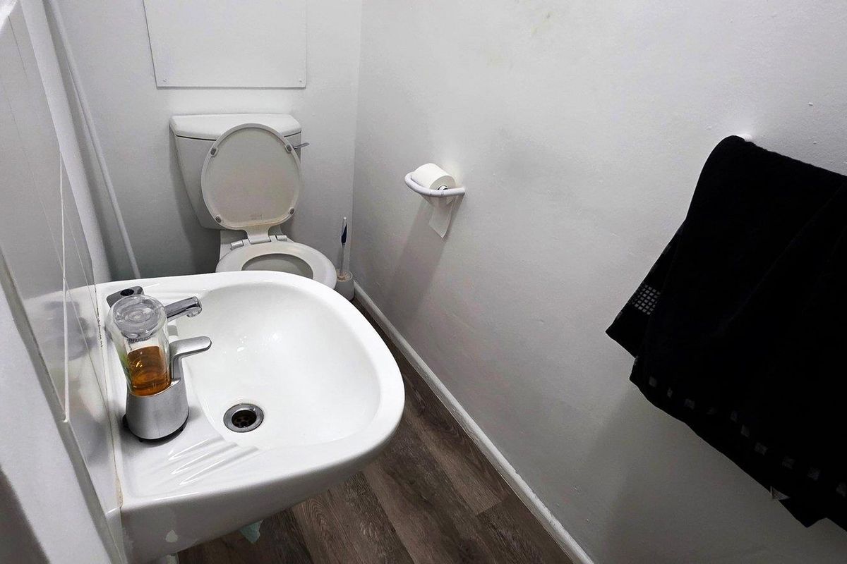 A compact office restroom featuring a wall-mounted basin and a standard toilet suite with wood-look vinyl flooring.