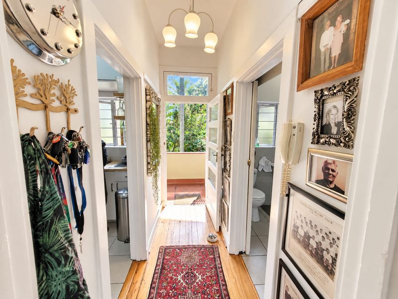 A bright hallway featuring polished hardwood flooring, leading towards an exterior door with a transom window, providing access to an outdoor space.