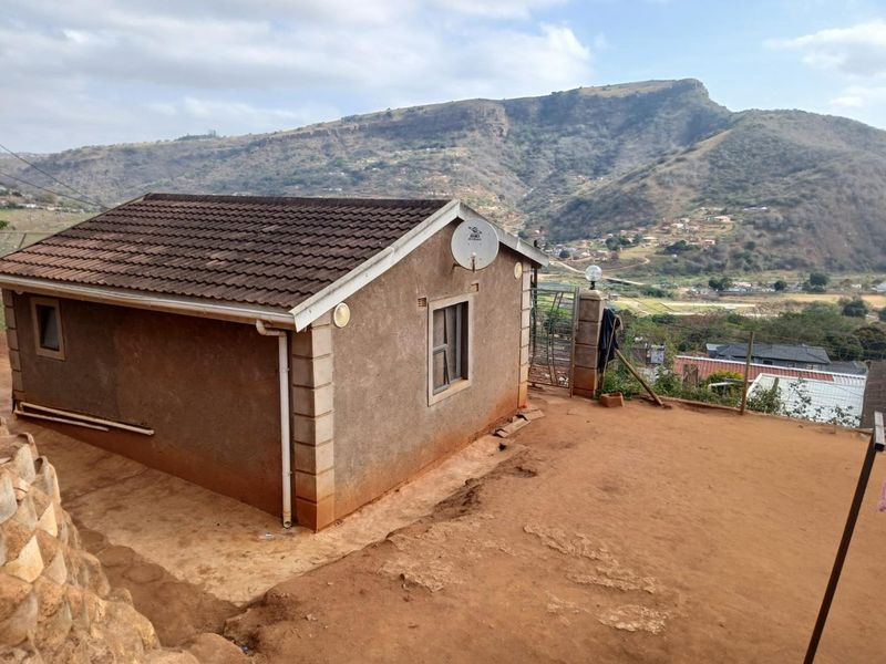 Rear view of the property featuring a tiled roof, satellite dish, and surrounding unpaved yard with scenic mountain views.