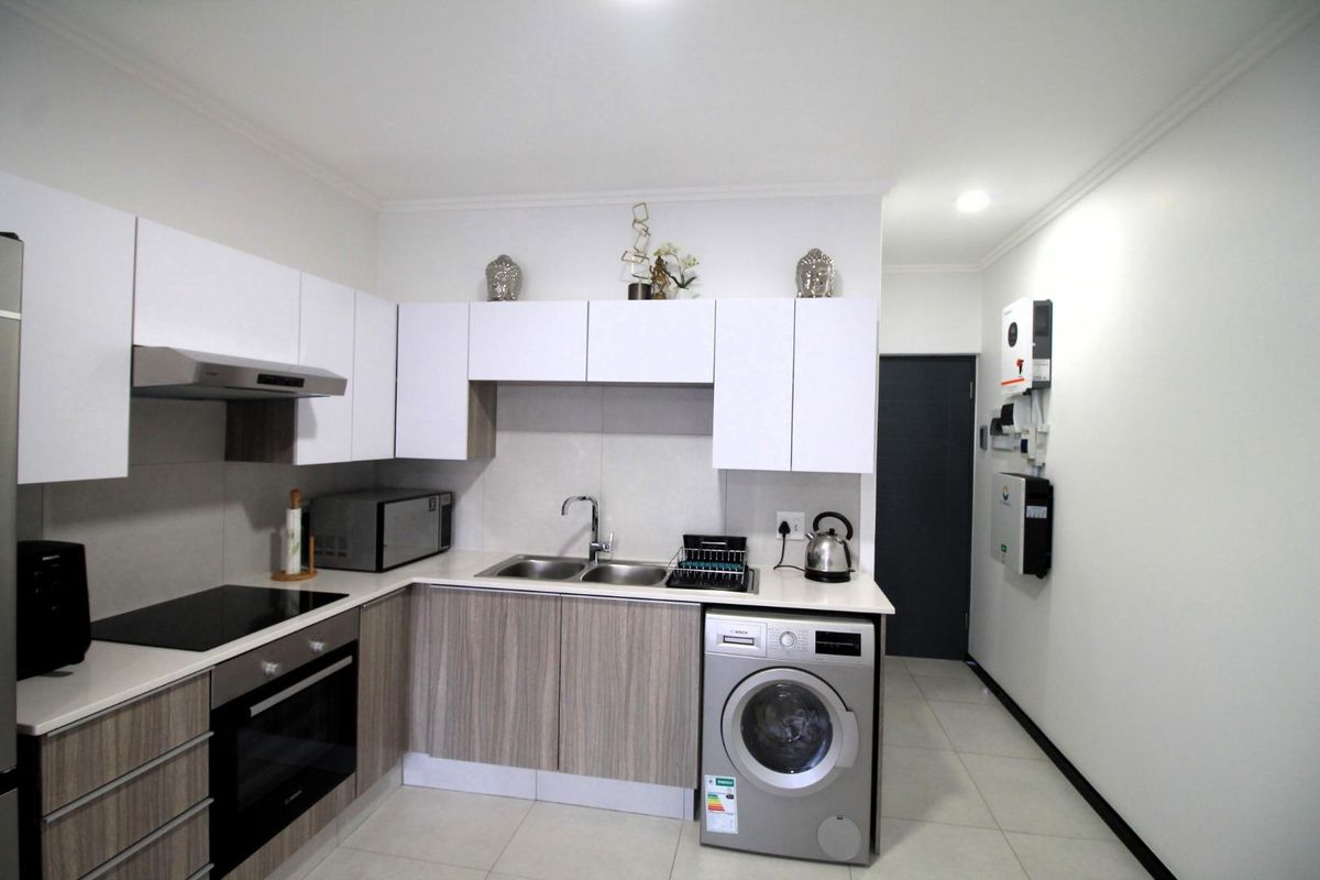Modern kitchen featuring sleek two-tone cabinetry, integrated oven, hob, extractor fan, and dedicated space for a washing machine.