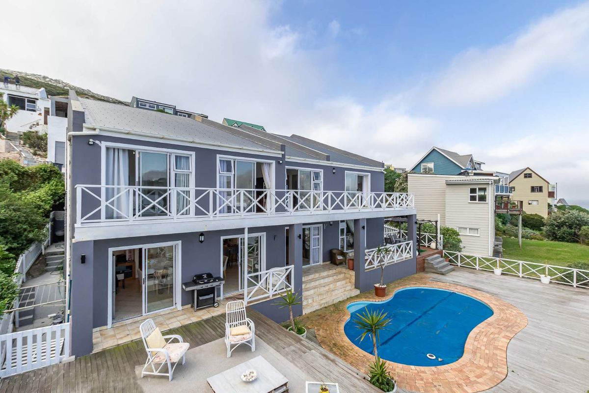 Rear view of a multi-level house featuring a swimming pool, expansive timber decking, and a balcony with white railings.