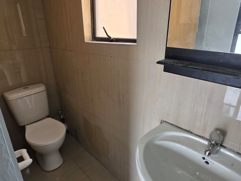 A compact bathroom featuring tiled walls and flooring, a standard toilet, and a wall-mounted washbasin with a mirror.