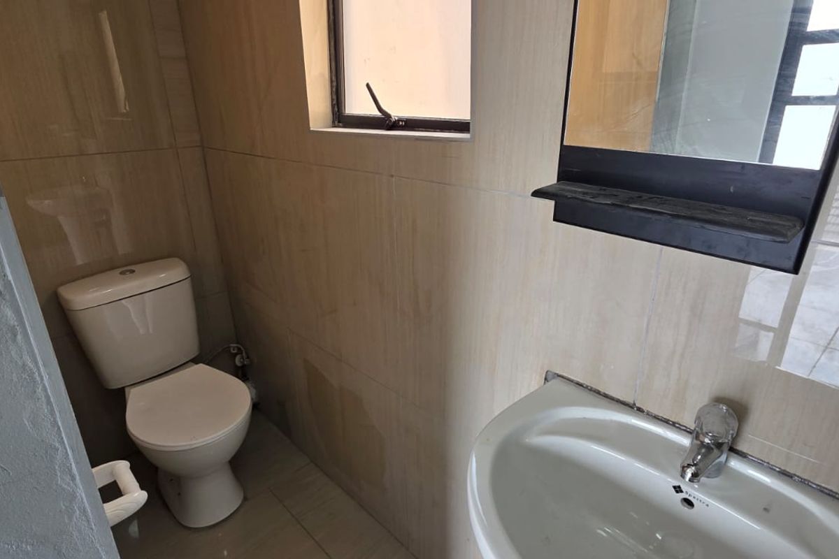 A compact bathroom featuring tiled walls and flooring, a standard toilet, and a wall-mounted washbasin with a mirror.