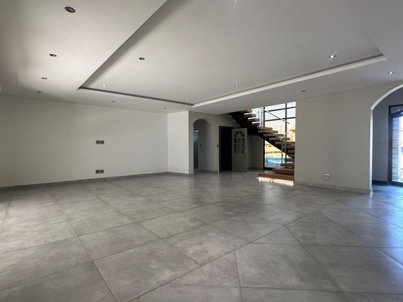 Spacious open-plan living area featuring modern large-format floor tiles, recessed ceiling lighting, and a striking floating staircase with a glass balustrade.