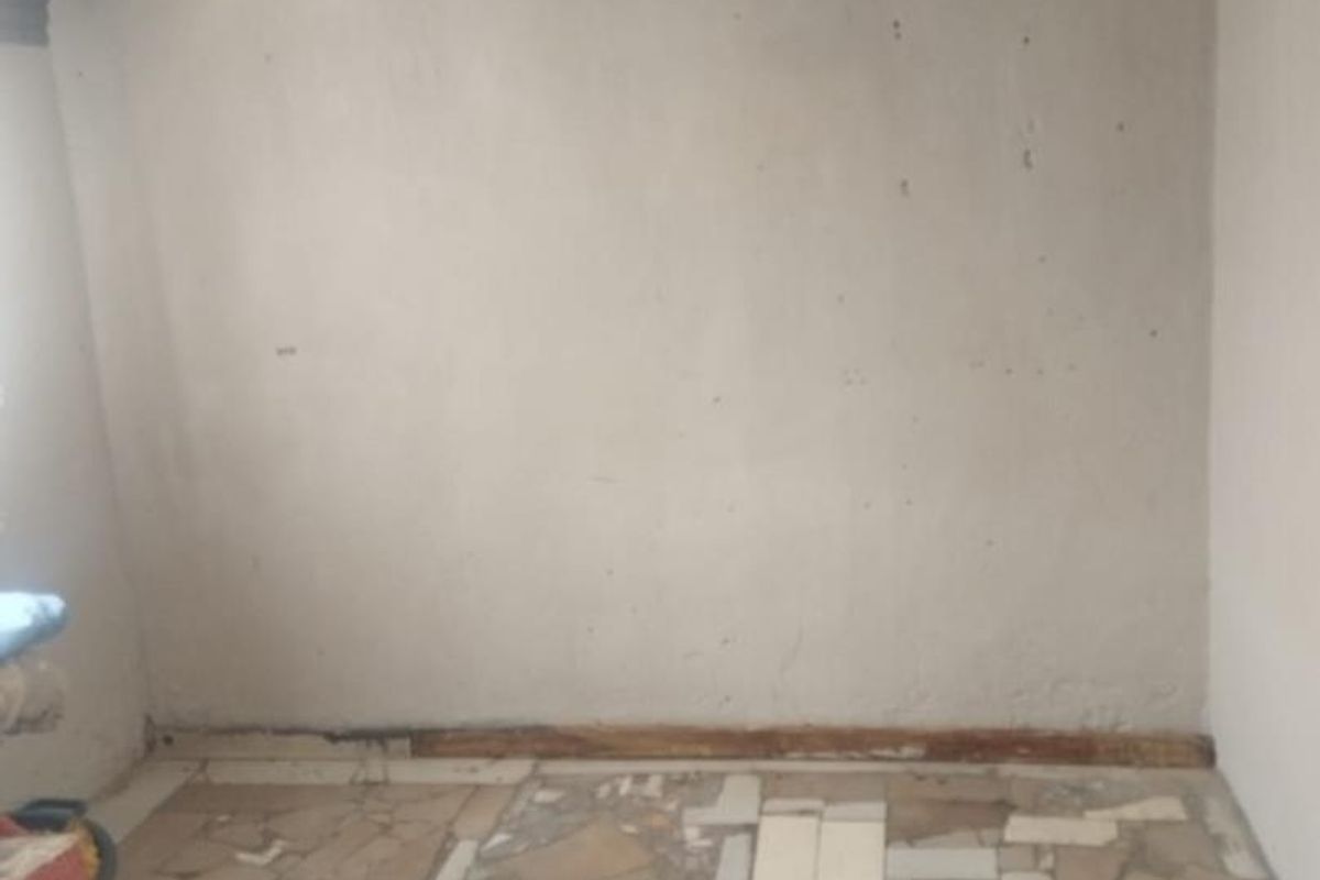 An interior room featuring a damaged mosaic-style tiled floor and unfinished wall surfaces, requiring significant renovation and repair.