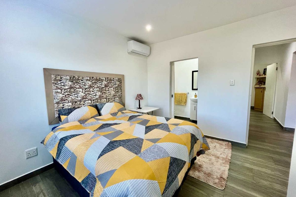 A well-maintained bedroom featuring wood-look flooring, a wall-mounted air conditioning unit, and direct access to an en-suite bathroom.
