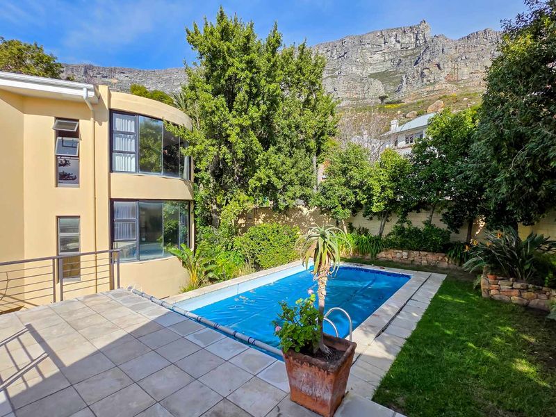 Outdoor pool area featuring a tiled patio, swimming pool, and mountain views, set within a landscaped garden with a curved architectural facade.