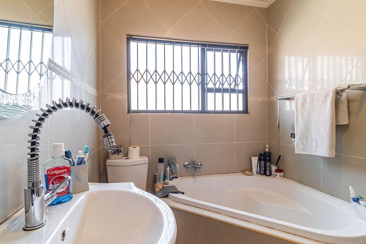 A functional bathroom featuring a corner bathtub, pedestal basin with a modern gooseneck faucet, and neutral wall tiling with security bars on the window.