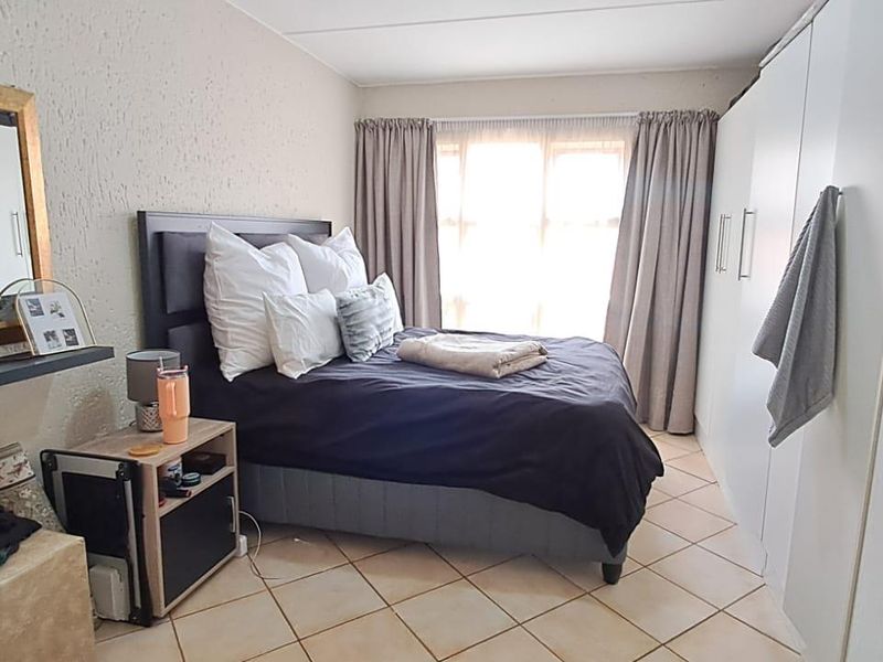 A functional bedroom featuring built-in cupboards, tiled flooring, and textured wall finishes, offering a practical layout with natural light.