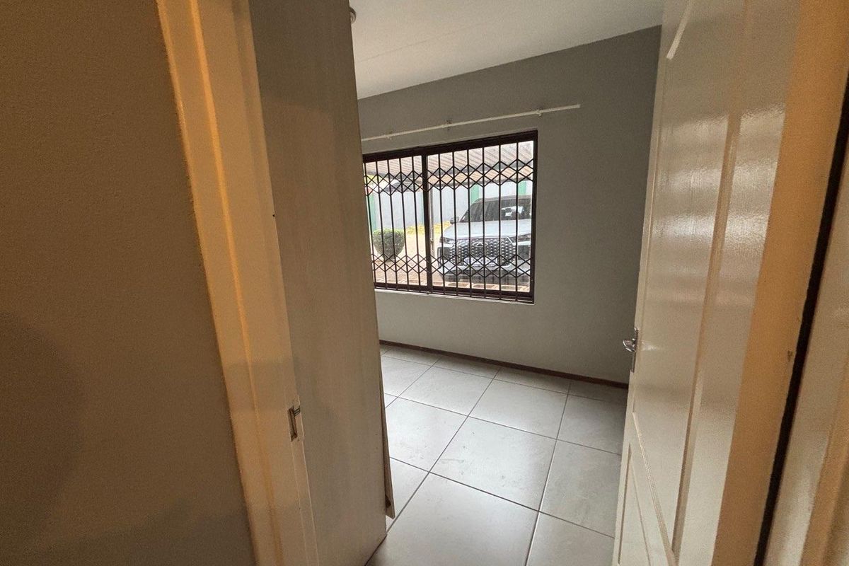 An empty bedroom featuring neutral tiled flooring and a window fitted with security bars.