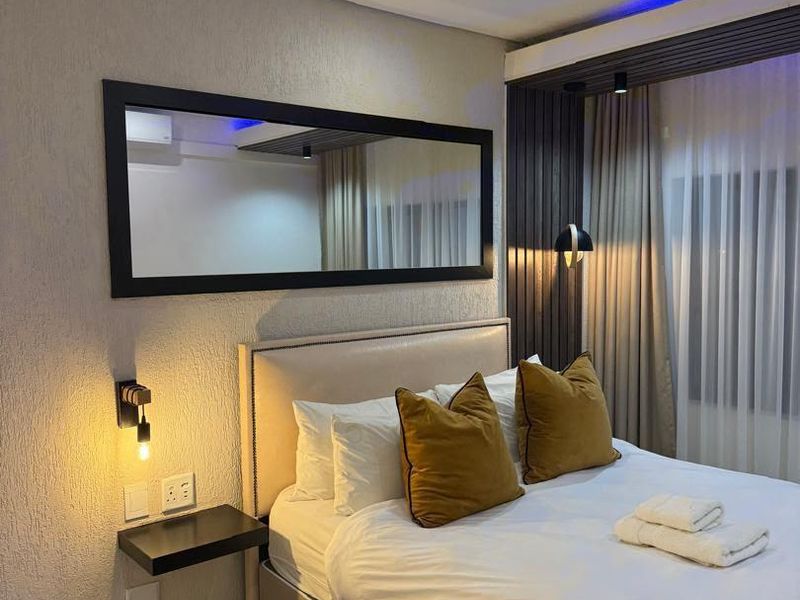A modern bedroom featuring a slatted timber accent wall, recessed downlighting, integrated LED strip lighting, and a wall-mounted bedside shelf.