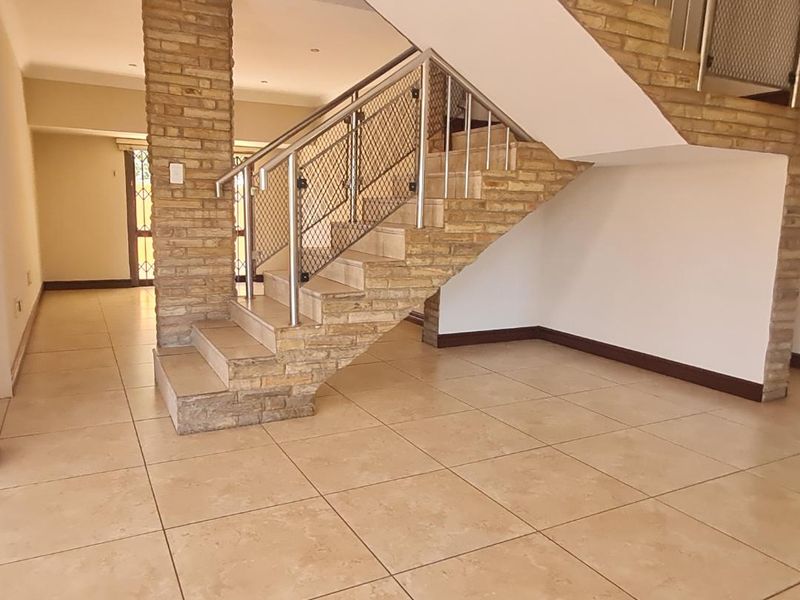 Spacious open-plan living area featuring a prominent staircase with stone cladding and modern metal balustrades, finished with neutral floor tiles.