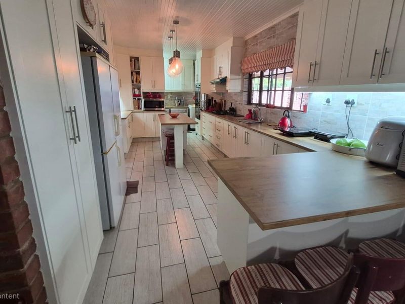 A spacious kitchen featuring white cabinetry, a central island, tiled flooring, and an exposed brick feature wall, offering a functional and well-lit workspace.