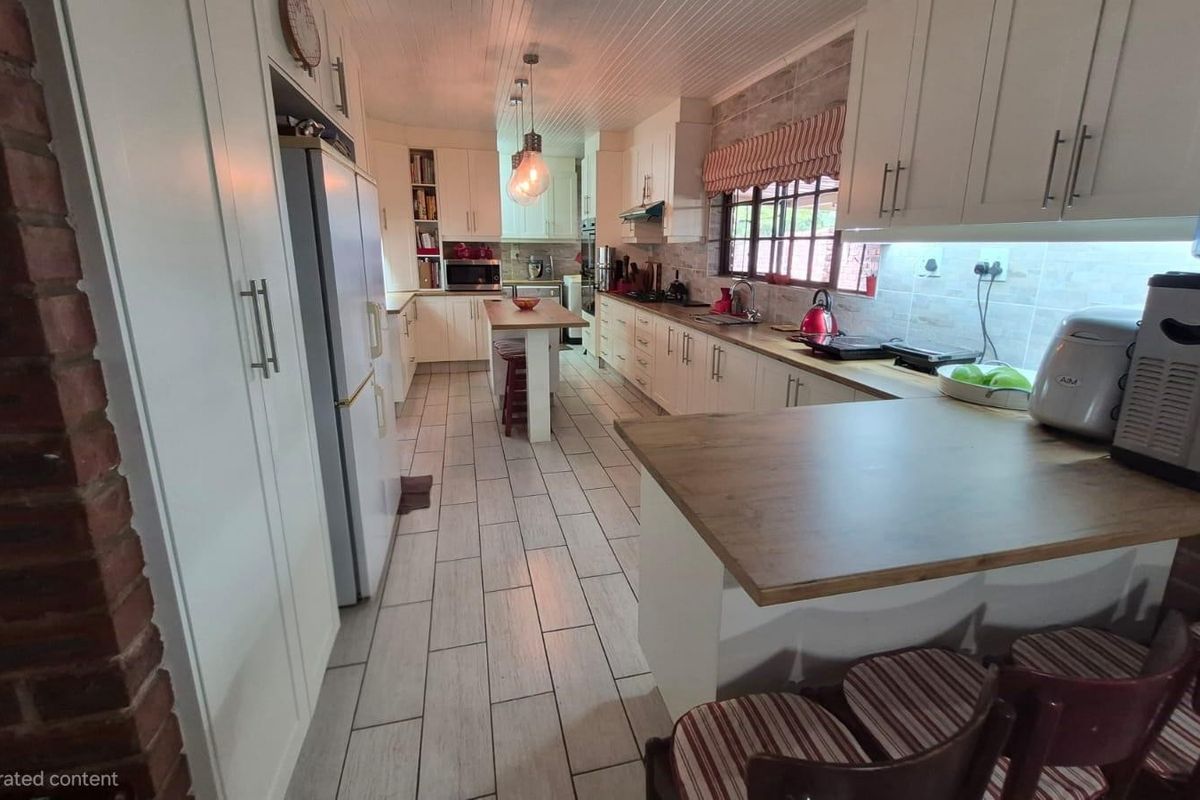 A spacious kitchen featuring white cabinetry, a central island, tiled flooring, and an exposed brick feature wall, offering a functional and well-lit workspace.