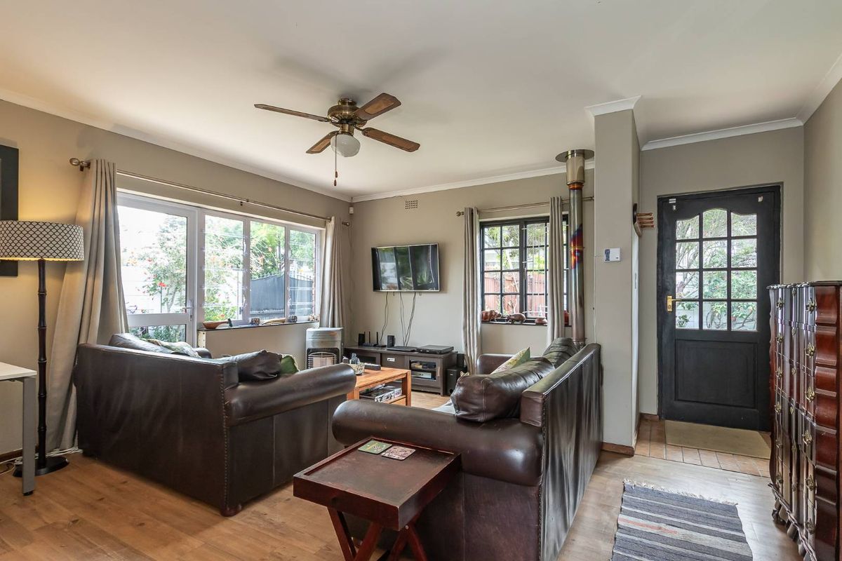 A comfortable living room featuring wood-look flooring, a ceiling fan, a wood-burning fireplace, and direct access to the garden through glass doors.