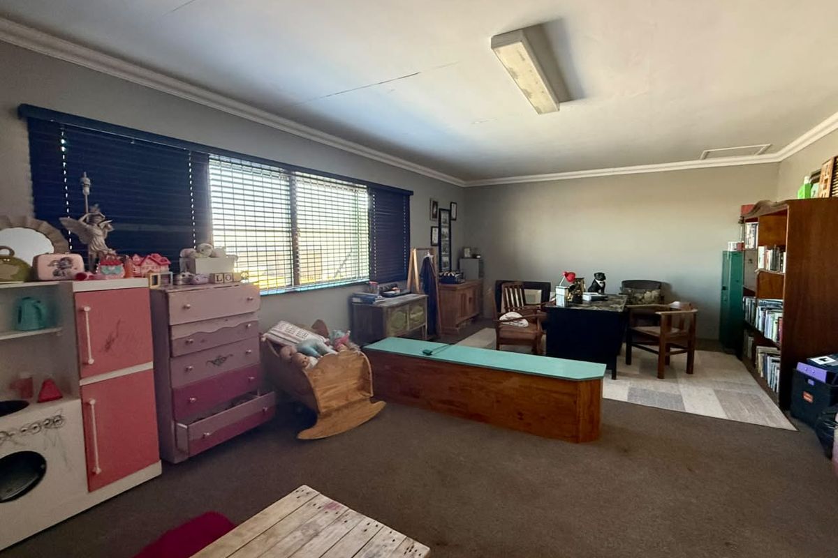 A spacious multi-purpose room featuring large windows with blinds, carpeted flooring, and a central fluorescent light fixture.