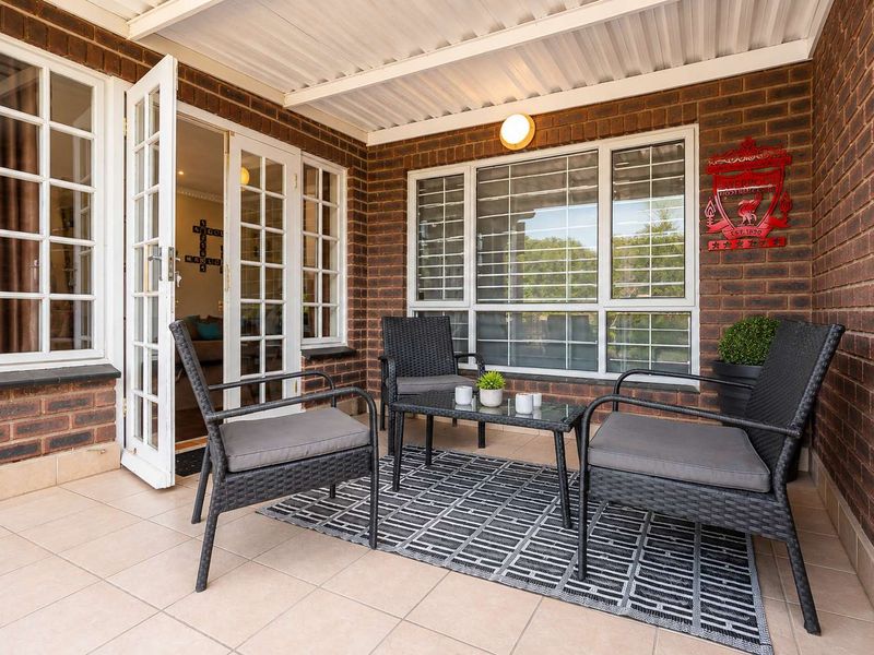 A covered outdoor patio area featuring brick walls, tiled flooring, and access to the interior through classic french doors.
