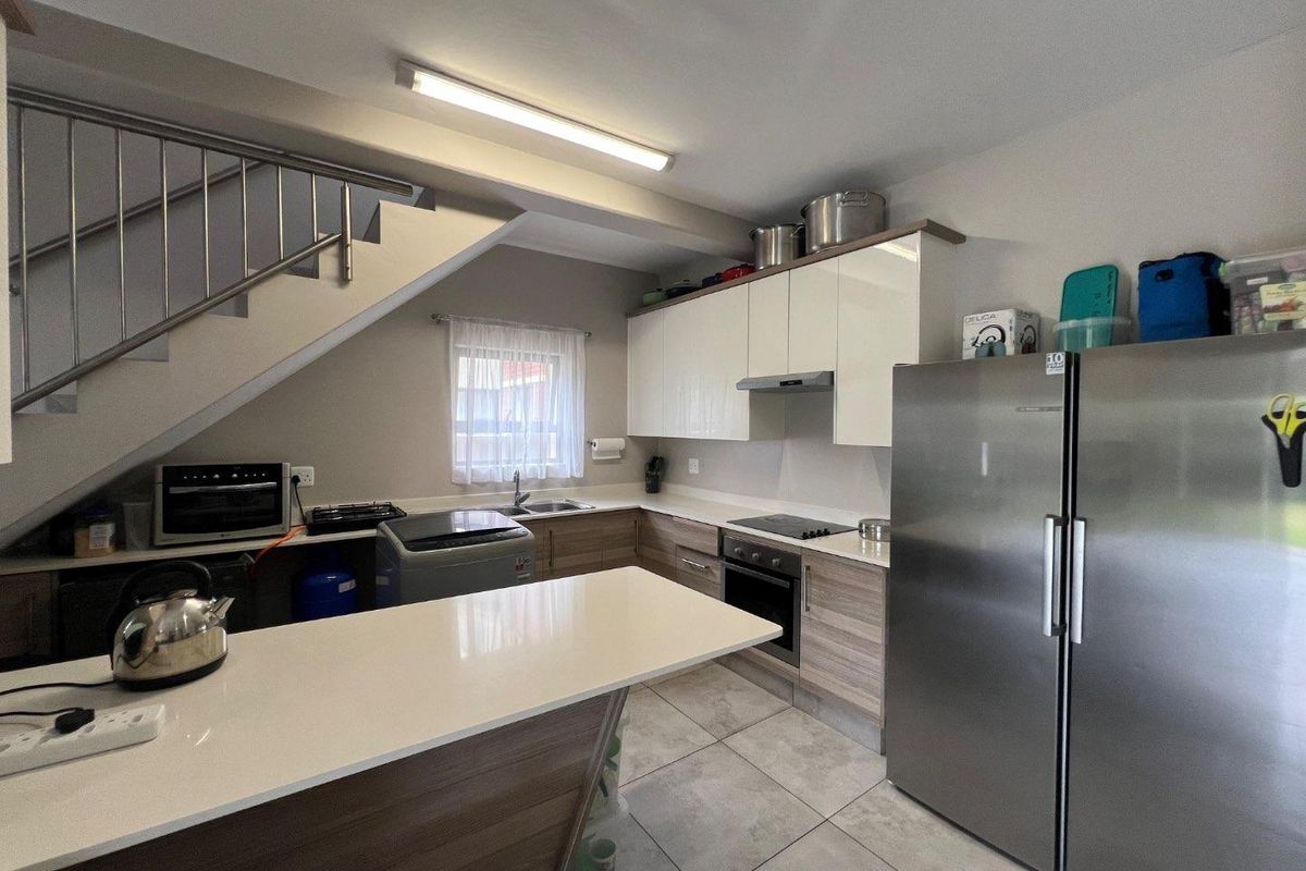 Modern kitchen featuring sleek cabinetry, stone countertops, integrated oven and hob, and a breakfast bar, conveniently located beneath the staircase.