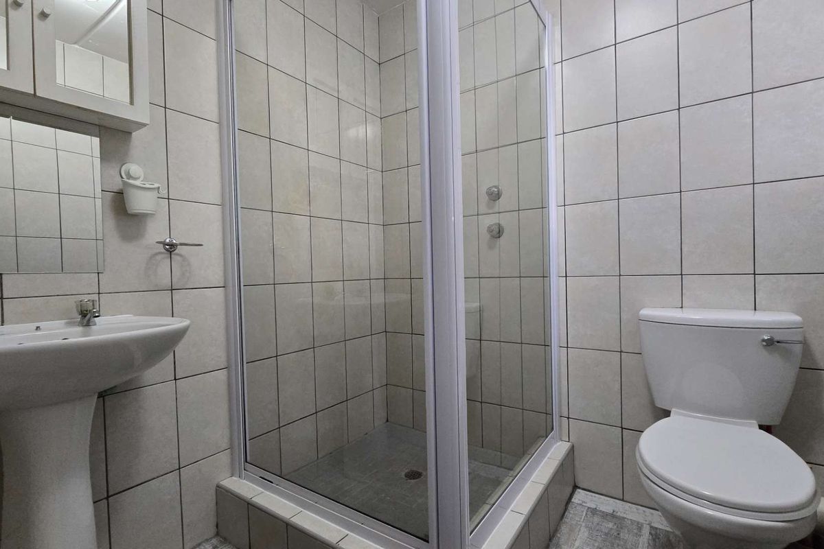 A functional bathroom featuring a pedestal basin, a glass-enclosed shower, and a toilet, finished with neutral wall tiling.