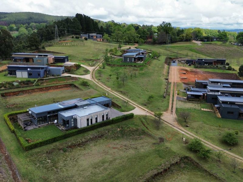 An aerial view of a modern residential estate featuring contemporary homes, manicured lawns, and established access roads within a scenic landscape.