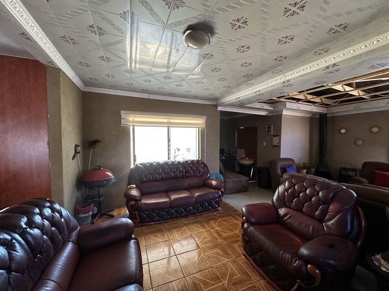 Spacious living area featuring tiled flooring and decorative ceiling tiles, currently requiring repairs to the ceiling structure and general cosmetic updates.