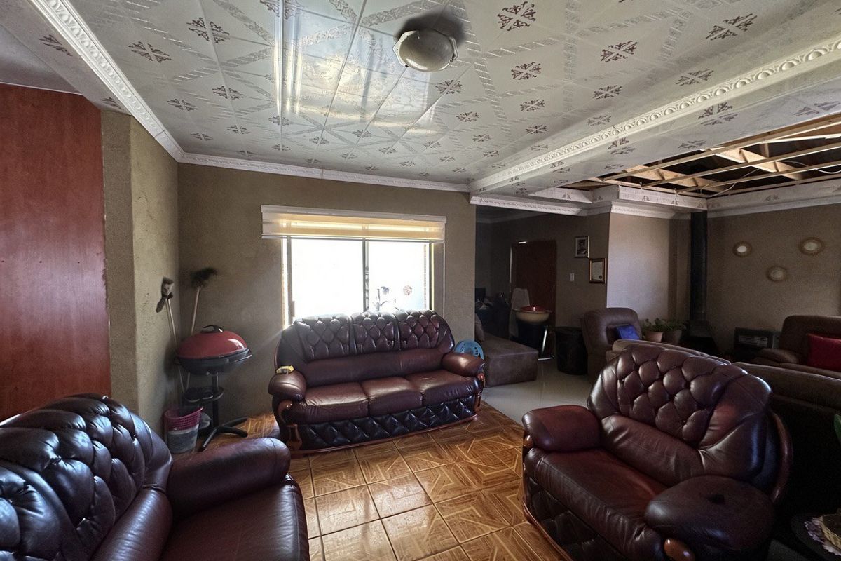 Spacious living area featuring tiled flooring and decorative ceiling tiles, currently requiring repairs to the ceiling structure and general cosmetic updates.