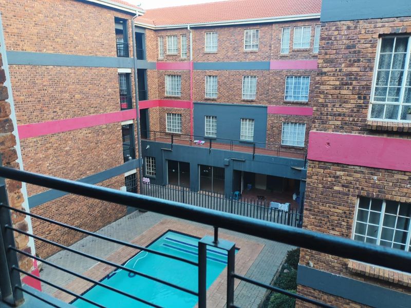 View of the apartment complex courtyard featuring a swimming pool, paved area, and multi-story brick building facade with security fencing.