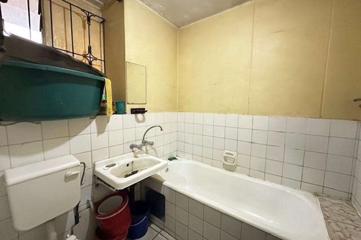 A dated bathroom featuring a standard bathtub, wall-mounted basin, and toilet, requiring significant renovation and cosmetic updates to improve functionality and aesthetic appeal.