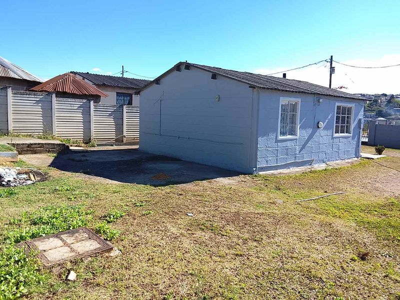 Rear view of a detached house featuring concrete block construction, a corrugated metal roof, and a surrounding yard with precast boundary walling.