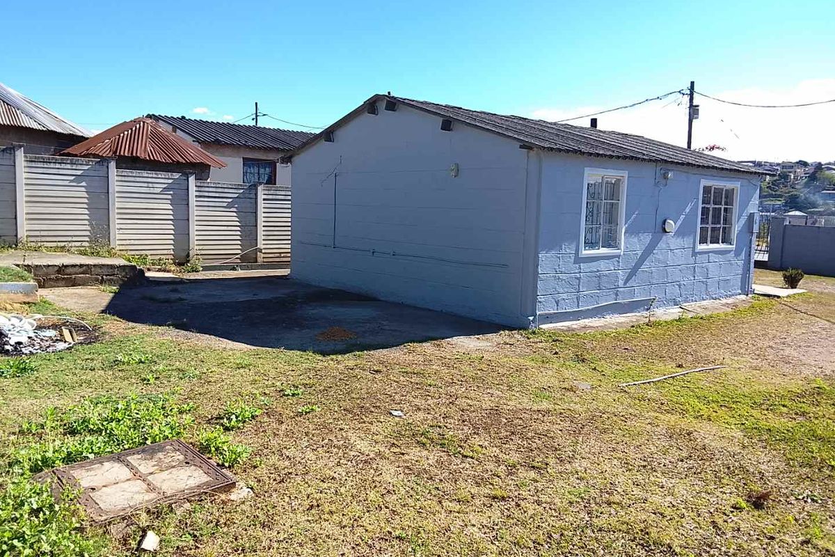 Rear view of a detached house featuring concrete block construction, a corrugated metal roof, and a surrounding yard with precast boundary walling.