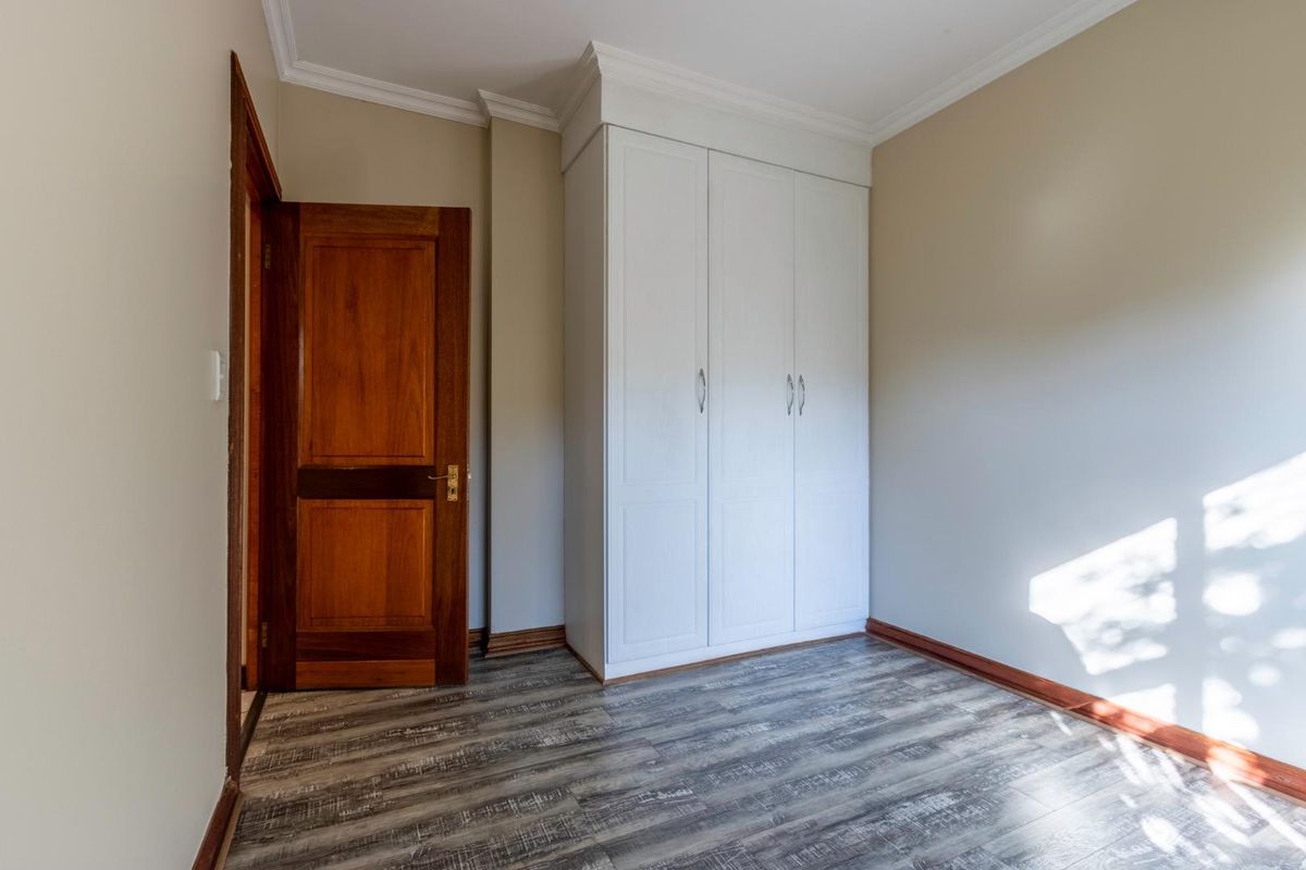 A bright bedroom featuring modern wood-look laminate flooring, a built-in white wardrobe, and a classic wooden door with matching skirting boards.