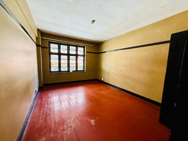 An empty bedroom featuring original timber flooring, a multi-pane window, and classic picture rails, ready for renovation and modernization.
