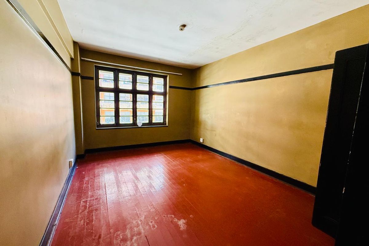 An empty bedroom featuring original timber flooring, a multi-pane window, and classic picture rails, ready for renovation and modernization.