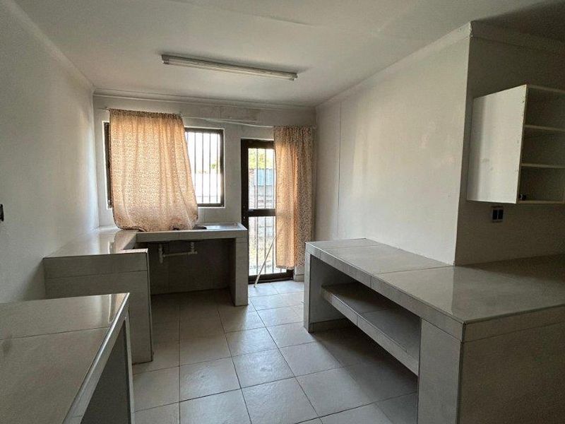A functional, empty kitchen space featuring tiled countertops, built-in shelving, and direct access to the exterior via a security gate.
