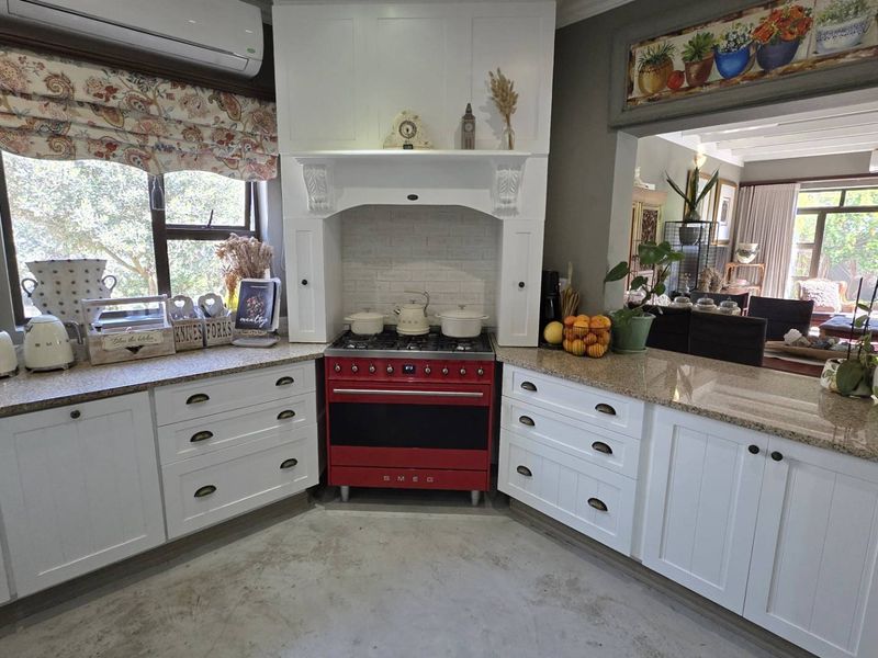A well-appointed kitchen featuring white cabinetry, granite countertops, and a prominent red Smeg gas range with a decorative extractor hood.