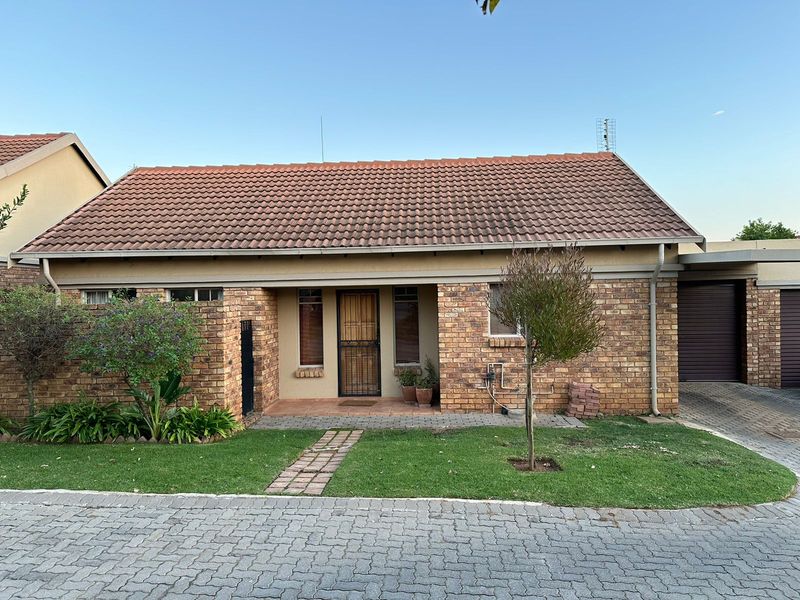 Front view of a face brick apartment featuring a tiled roof, secure entrance gate, paved walkway, and an attached garage.