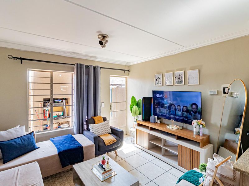 A cozy living room featuring tiled flooring, neutral wall tones, and a window fitted with security bars, providing a functional and comfortable living space.