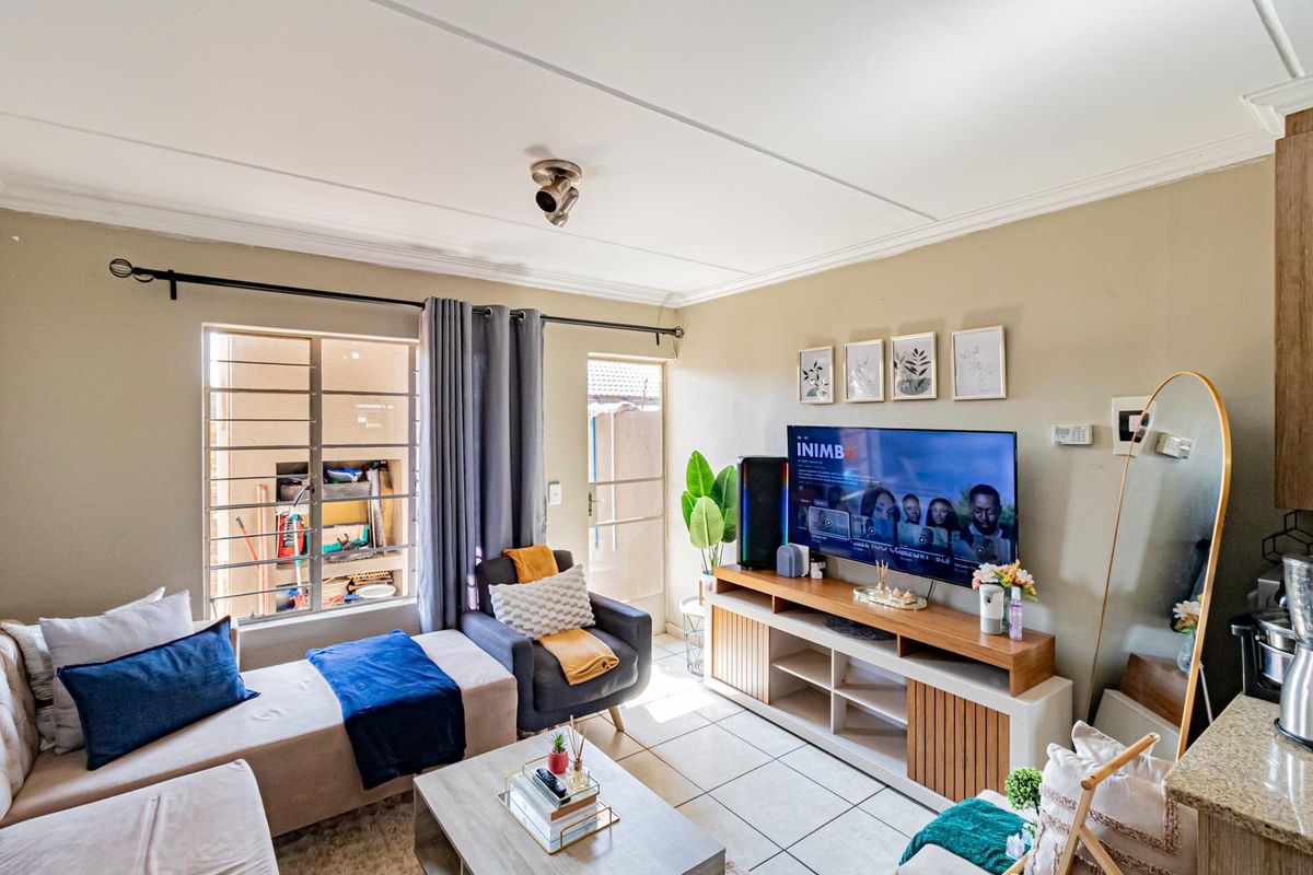 A cozy living room featuring tiled flooring, neutral wall tones, and a window fitted with security bars, providing a functional and comfortable living space.