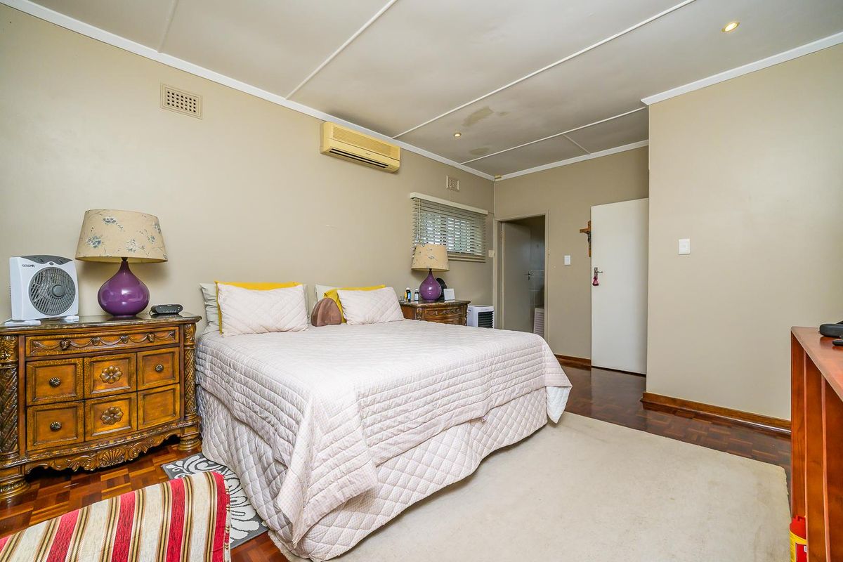 A bedroom featuring parquet flooring, a wall-mounted air conditioning unit, and a doorway leading to an en-suite bathroom.
