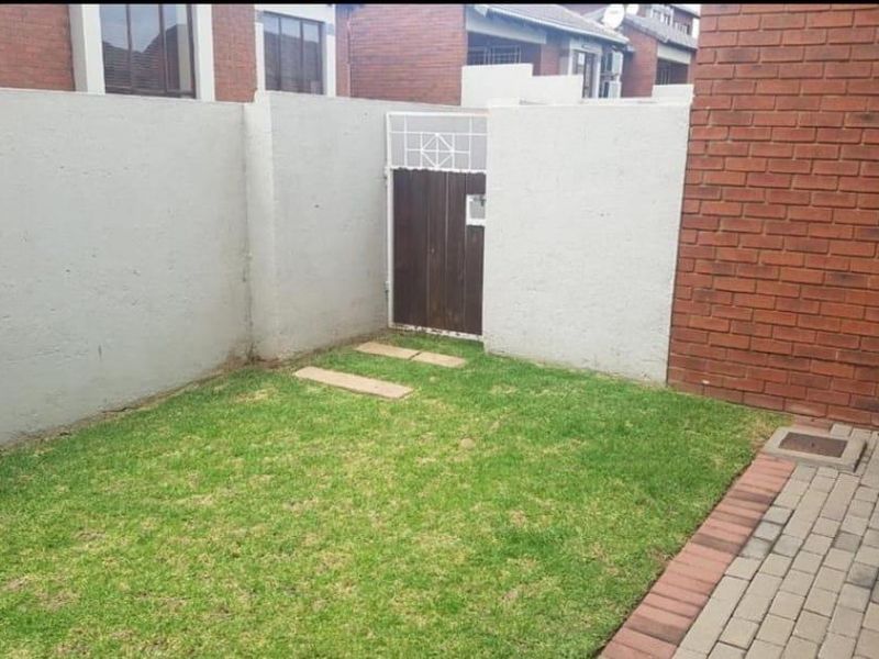 A private rear garden area featuring a small lawn, paved walkway, and enclosed boundary walls with a pedestrian access gate.