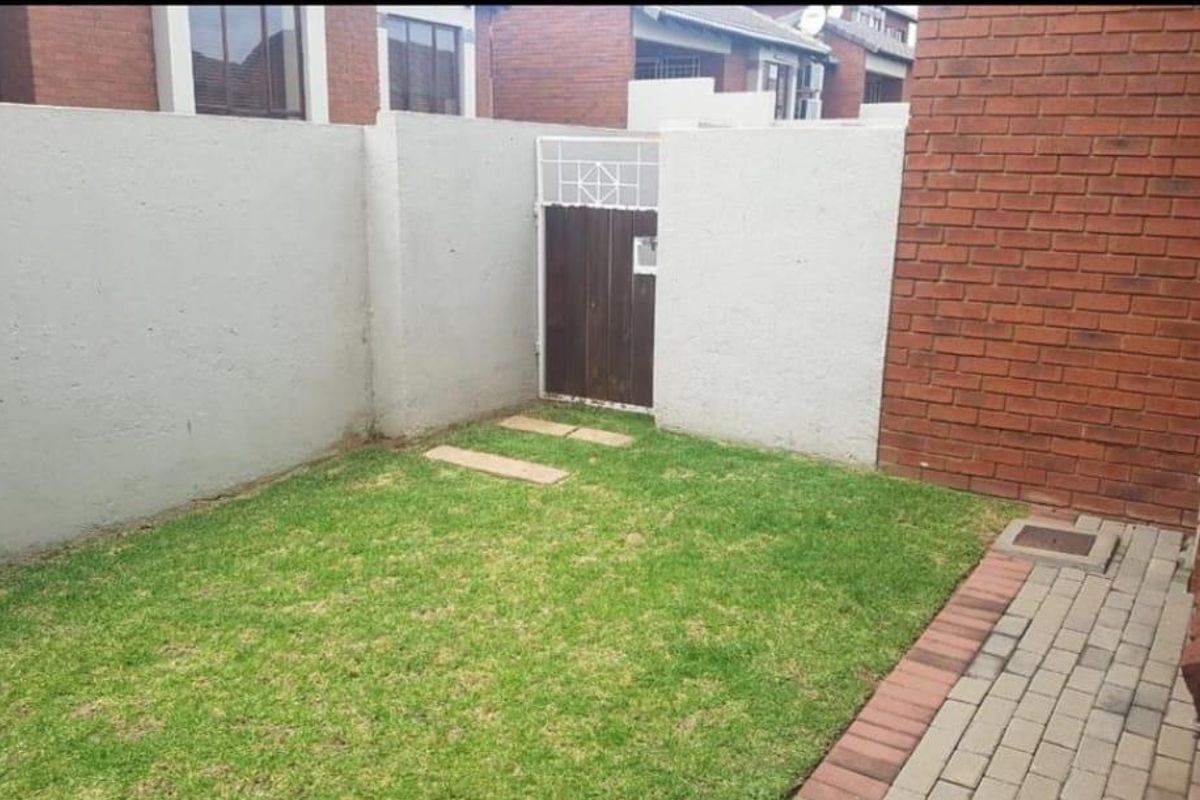 A private rear garden area featuring a small lawn, paved walkway, and enclosed boundary walls with a pedestrian access gate.