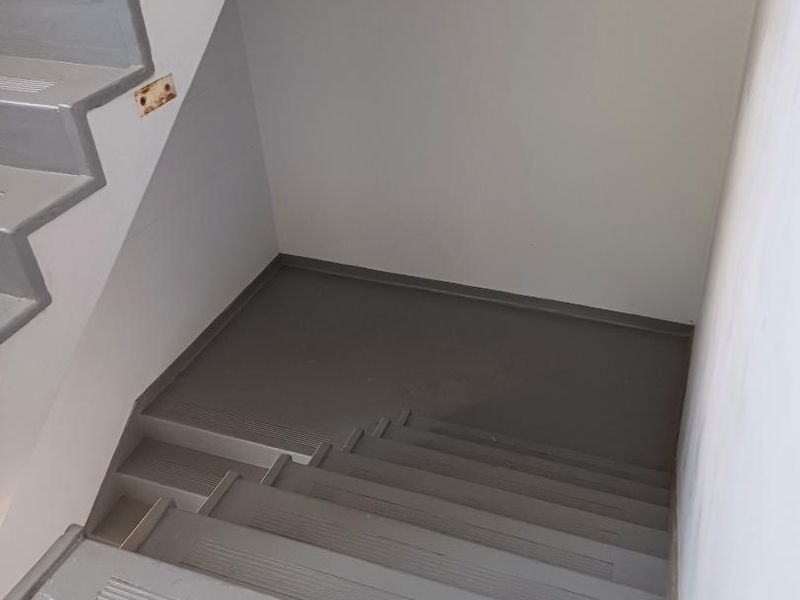 A functional interior staircase with painted concrete steps and a landing, featuring a wall-mounted light fixture and an exposed electrical outlet.