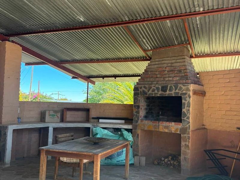 Covered outdoor entertainment area featuring a stone-clad built-in braai, concrete prep counters, and durable stone flooring under a corrugated metal roof.