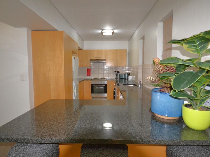 A functional kitchen featuring wooden cabinetry, granite countertops, a tiled backsplash, and integrated appliances, including a built-in oven and extractor fan.