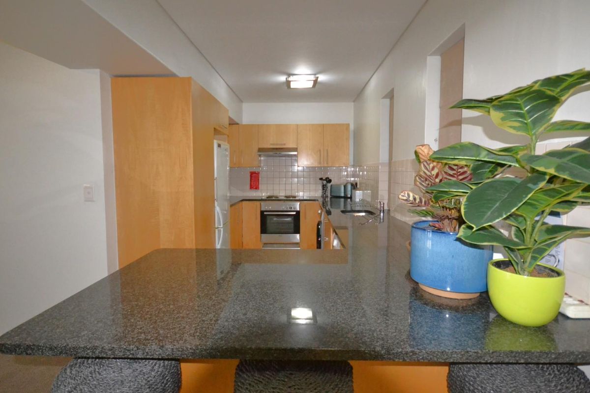 A functional kitchen featuring wooden cabinetry, granite countertops, a tiled backsplash, and integrated appliances, including a built-in oven and extractor fan.