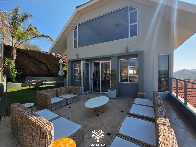 Spacious outdoor patio area featuring tiled flooring, glass sliding doors, and a metal balustrade, overlooking the surrounding landscape.