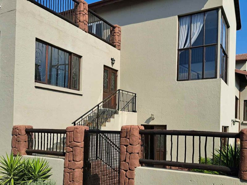 Front elevation of a multi-level house featuring stone-clad pillars, wrought iron fencing, an external staircase, and a balcony.