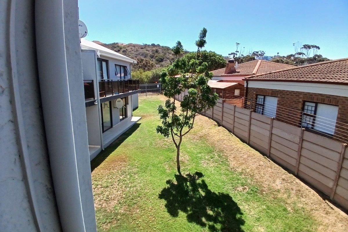 View of the rear garden area featuring a lawn, precast boundary wall with electric fencing, and a view of the adjacent property's exterior.